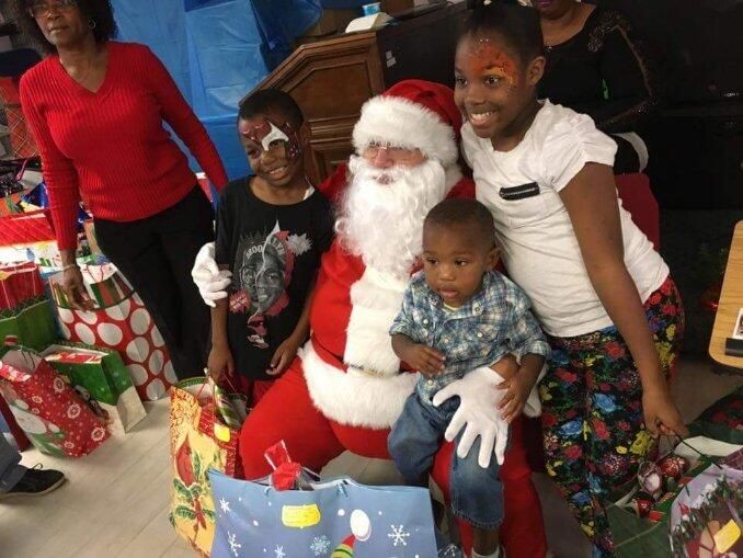 Santa Claus sitting with children and surrounded by Christmas gifts in festive wrapping paper.